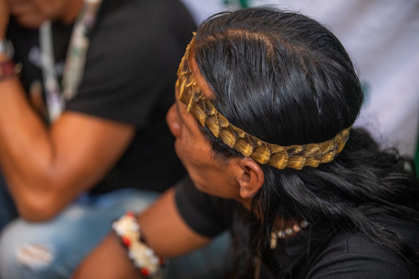Líder indígena de espaldas con una diadema de escamas doradas sobre el cabello negro