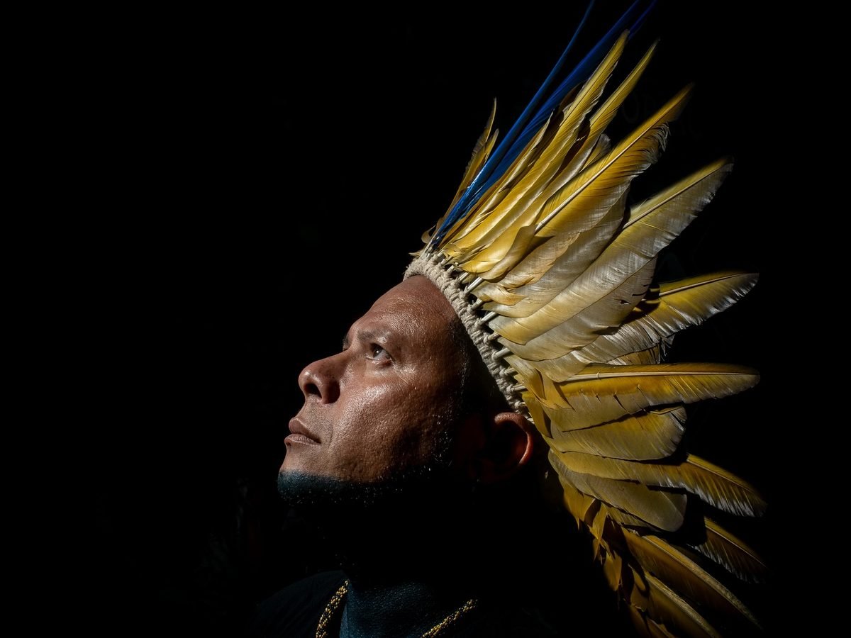 Retrato de un líder indígena con tocado de plumas amarillas y azules mirando hacia arriba